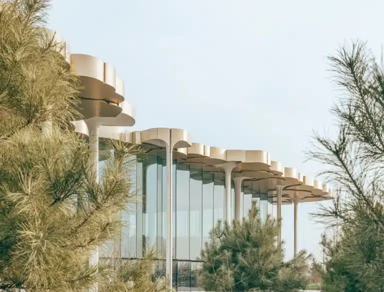 Modern building with layered canopy structures and glass walls framed by pine trees under daylight.