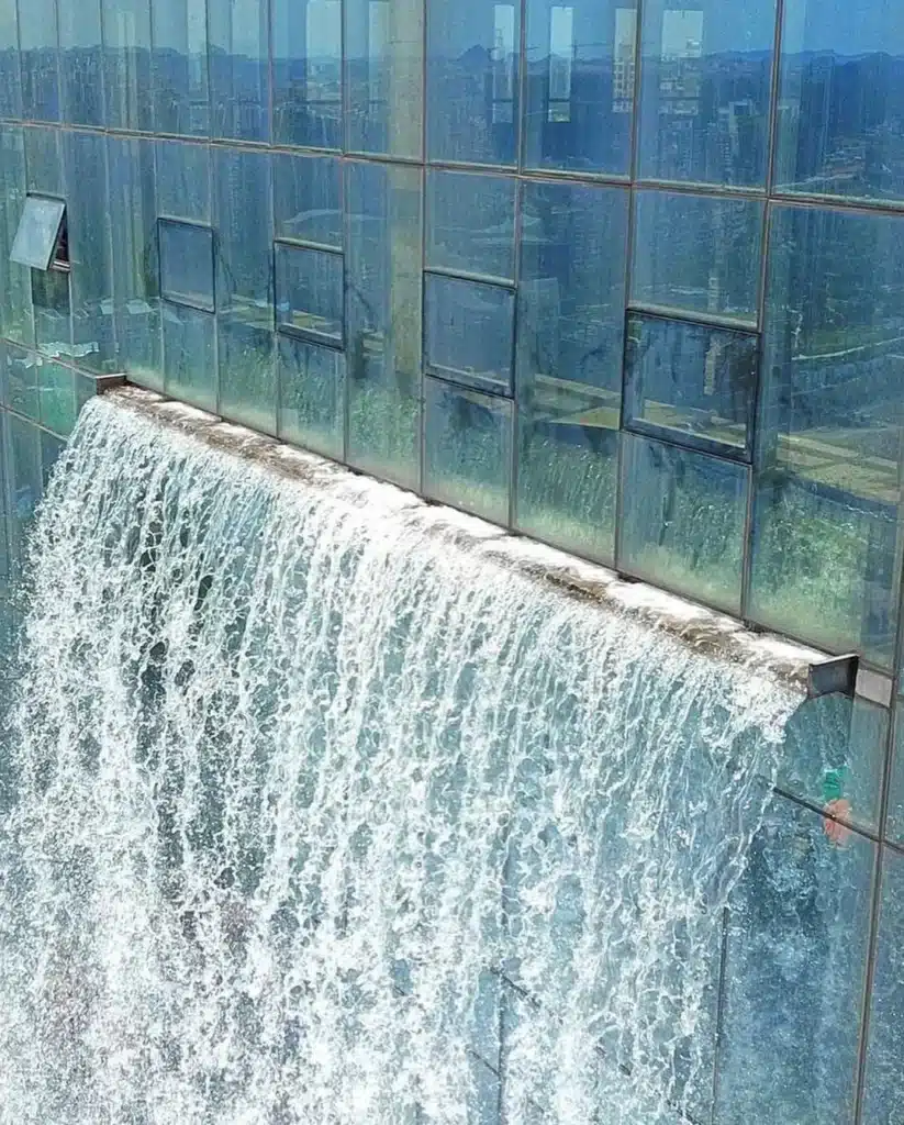 لقطة مقربة ناطحة سحاب بشلال وهو يتدفق على واجهة الزجاج لبرج ليبيان الدولي في قوييانغ، الصين. تتدفق المياه فوق حافة خرسانية مع ظهور انعكاسات المدينة في الألواح.
