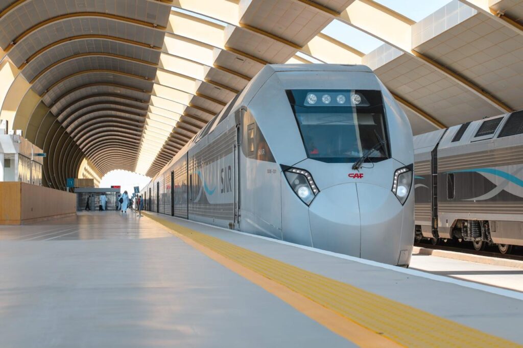 A CAF high-speed train stands at a shaded station platform, illustrating the integrated platform cover design with the High-Speed Electric Rail Link track.