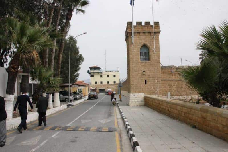 The former British High Commission in Nicosia before renovation, featuring a historic stone tower and tree-lined street, within the context of the new carbon-neutral diplomatic headquarters project.