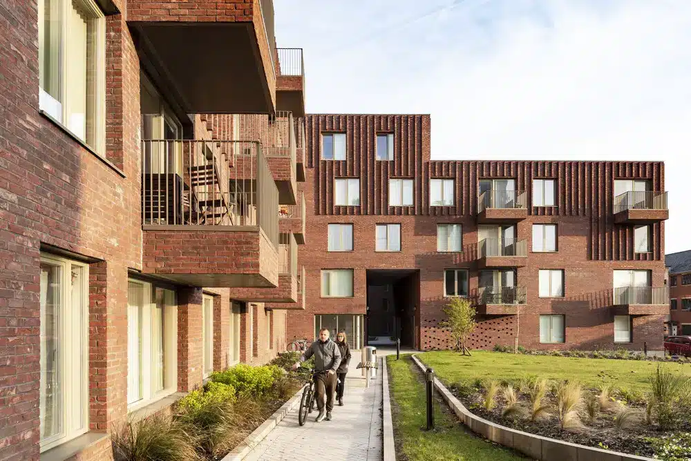 A modern residential [building] with red brick fa&ccedil;ades and vertical partitions, showing sustainable [design] and the integration of pedestrian and cycling paths in Architectural Regeneration in Manchester.