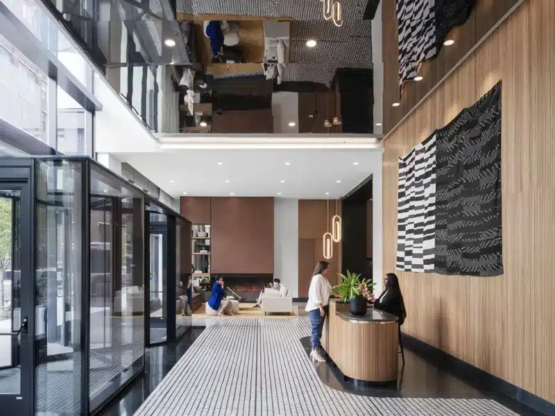 Modern lobby of Coppia Tower in Chicago, featuring a double-height ceiling, wood-paneled walls, contemporary art, and a communal lounge with fireplace and concierge desk.