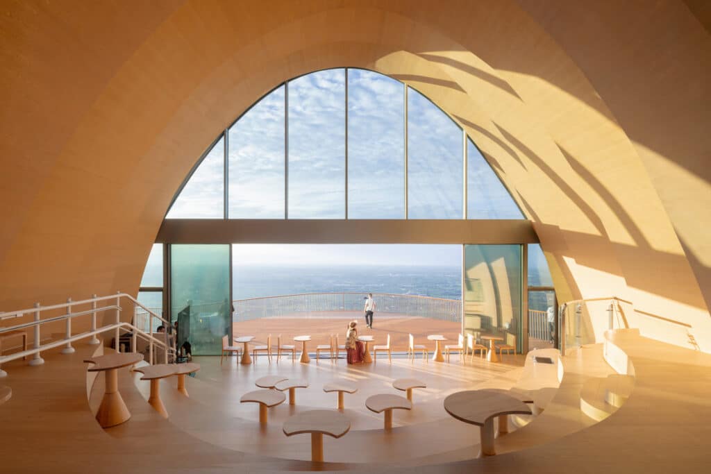 Interior of Pujiang Platform in Chengdu, a timber-clad arched hall with large glass windows overlooking plains, featuring curved wooden seating that follows the spatial geometry.