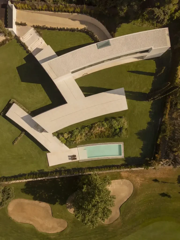 A house that melts into the garden: aerial view of a modern villa in Madrid flowing between golf course grounds through curved architectural lines and extended green spaces.