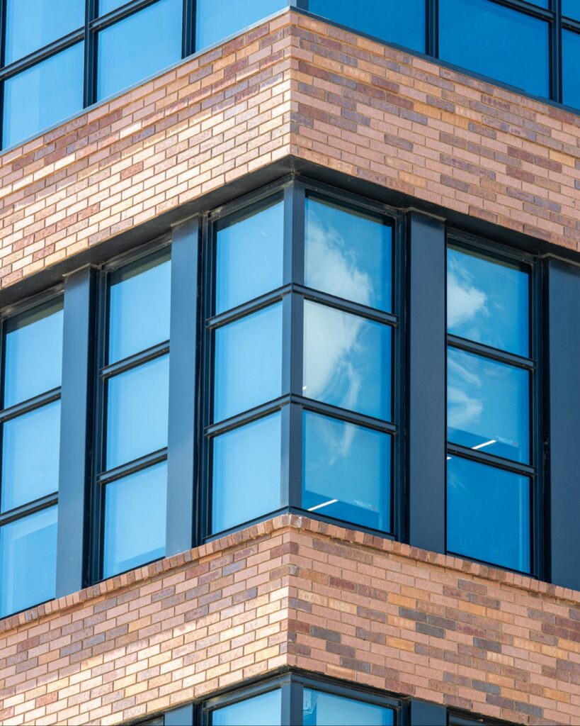 Close up of a building corner in Austin featuring layered brickwork and black-framed windows reflecting the sky, highlighting material texture and structural detail.