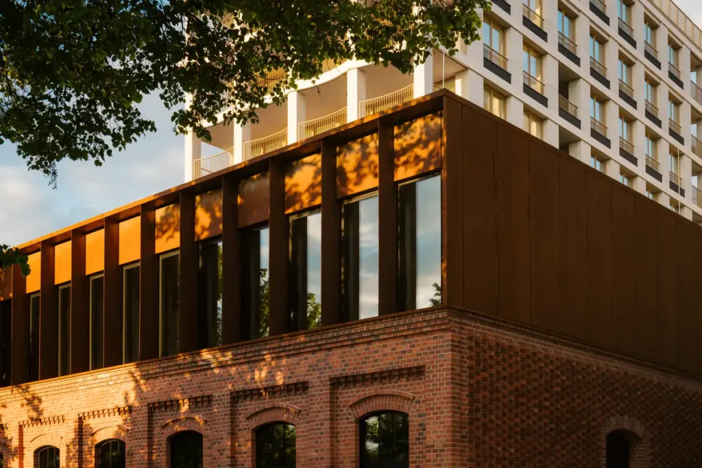 Detail of New Port residential development in Bydgoszcz, showing a modern dark facade with vertical window frames above a preserved red brick factory building at sunset.