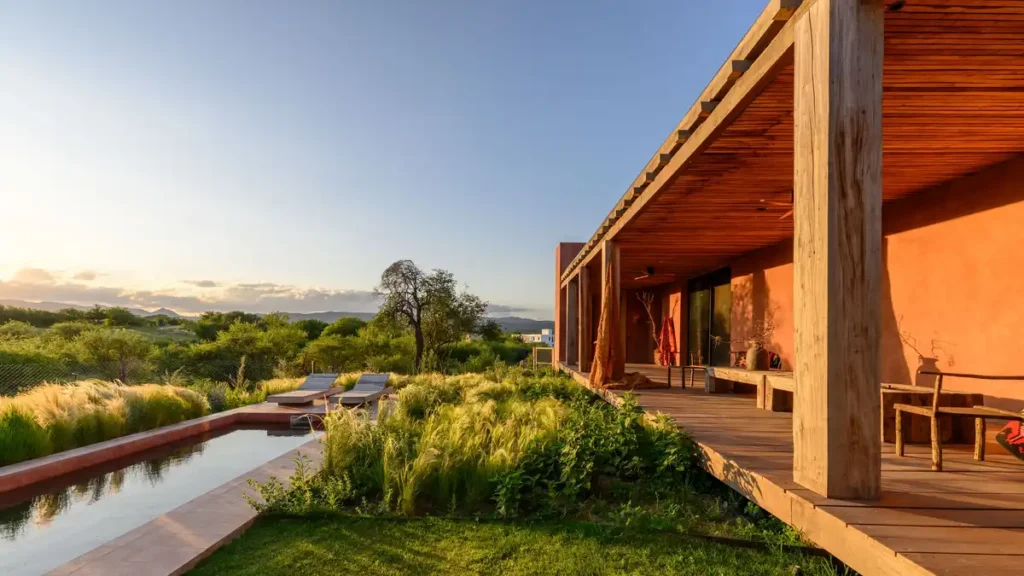 Wooden deck overlooks rolling hills, pool mirrors sunset glow above swaying grasses.