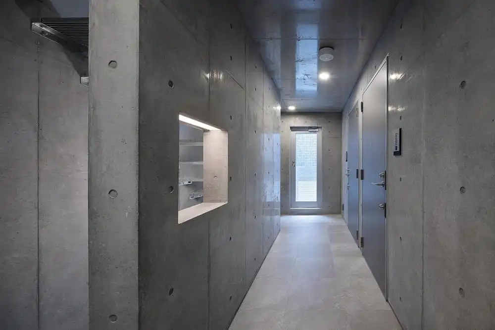 Interior hallway of Escenario Hanabusayama in Tokyo, showing exposed concrete walls, recessed lighting, and minimalist doorways.