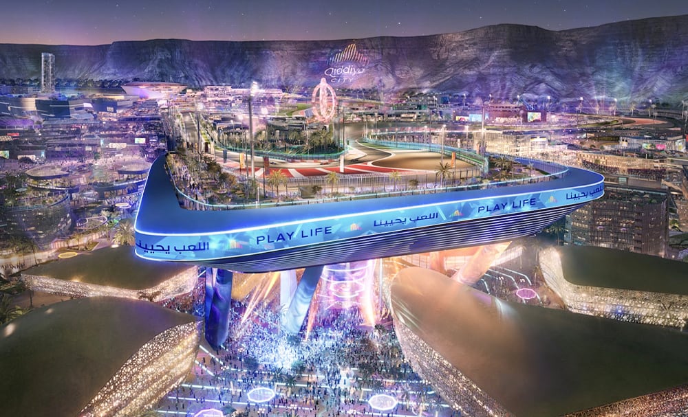 Night rendering of Qiddiya City&rsquo;s central plaza with illuminated pedestrian bridge, event space, and mountain backdrop featuring the Qiddiya logo.