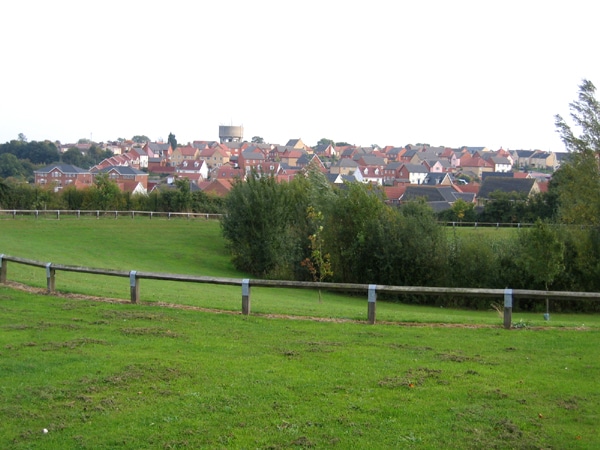 A wide-angle view of green fields and a residential town in west Suffolk, UK, showing the rural landscape between Newmarket and Haverhill &mdash; the proposed site for the Forest City development.