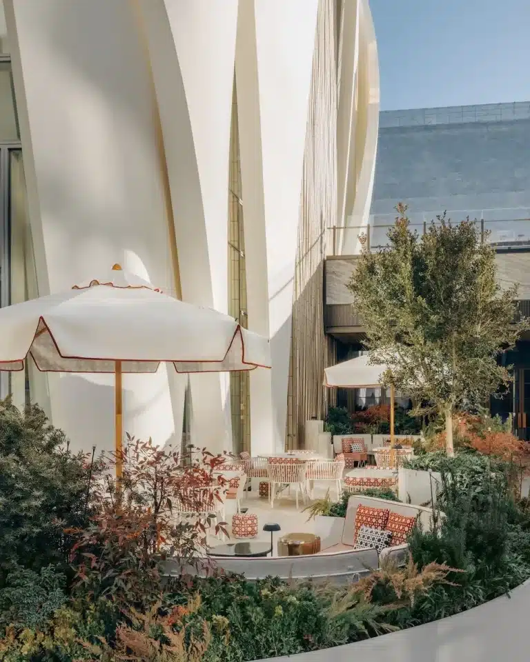 Outdoor seating area at the Dior Beijing flagship store, featuring white umbrellas and patterned furniture nestled among greenery against the building’s sculptural white petal facade.