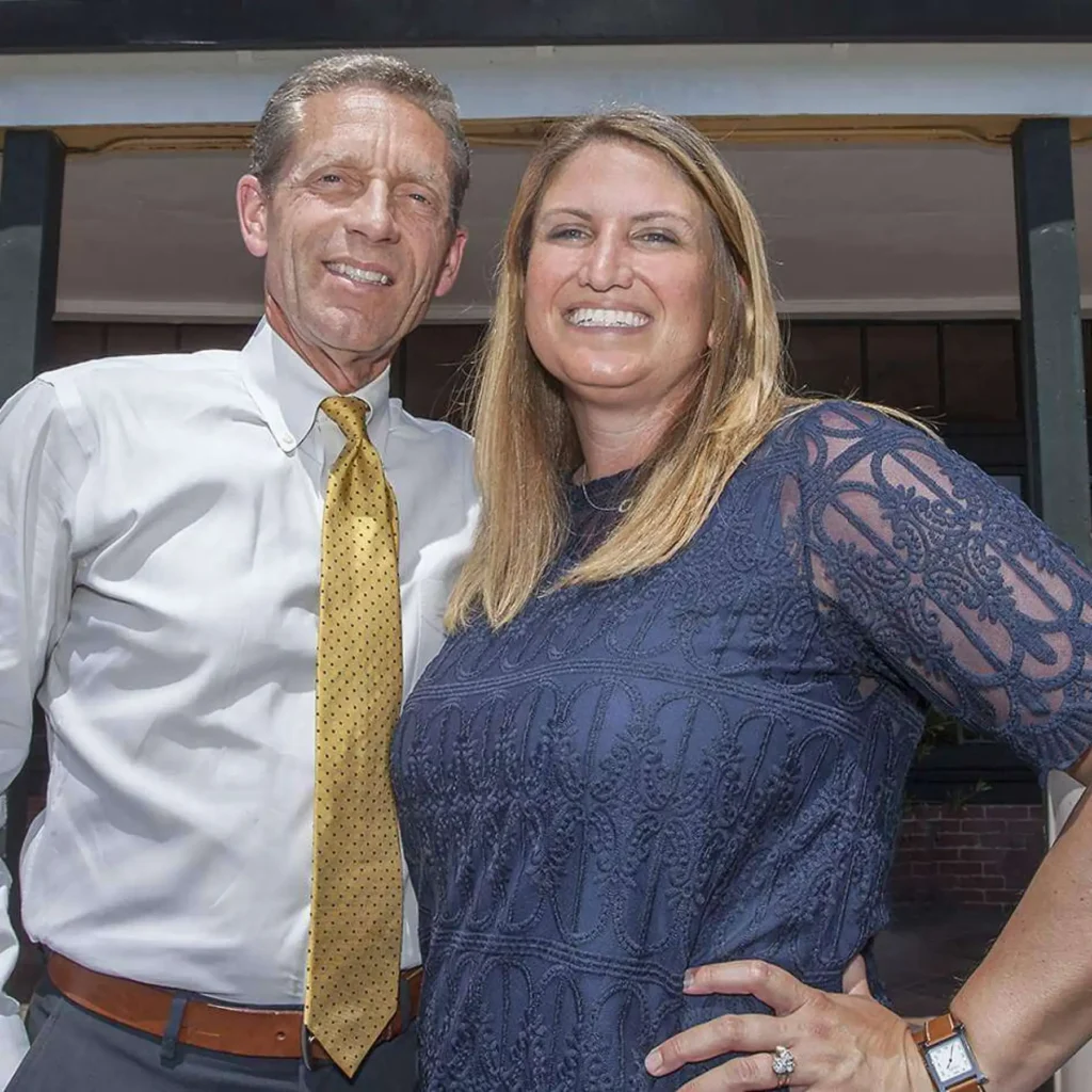 صورة مقربة لرجل في منتصف العمر بعينين زرقاوين وشعر رمادي، يرتدي سترة داكنة وربطة عنق صفراء منقوشة، وينظر قليلاً بعيداً عن الكاميرا. تظهر رأس شخص آخر خارج نطاق التركيز في المقدمة على اليسار.