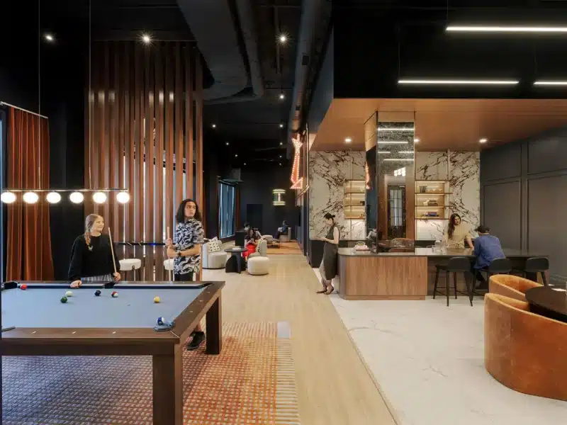 Residents enjoying the game room at Coppia Tower in Chicago, featuring a pool table, bar area with marble backsplash, and modern lounge seating.