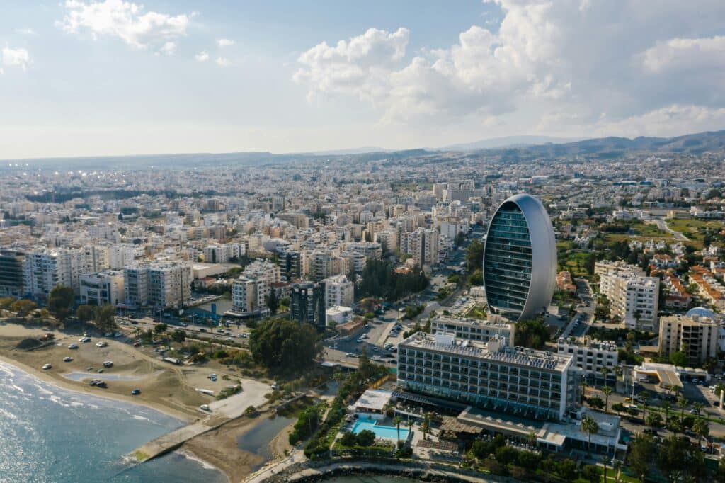 Aerial view of Nicosia, Cyprus, showcasing a distinctive arched architectural landmark amid residential blocks, with the seafront in the foreground and mountains in the distance.