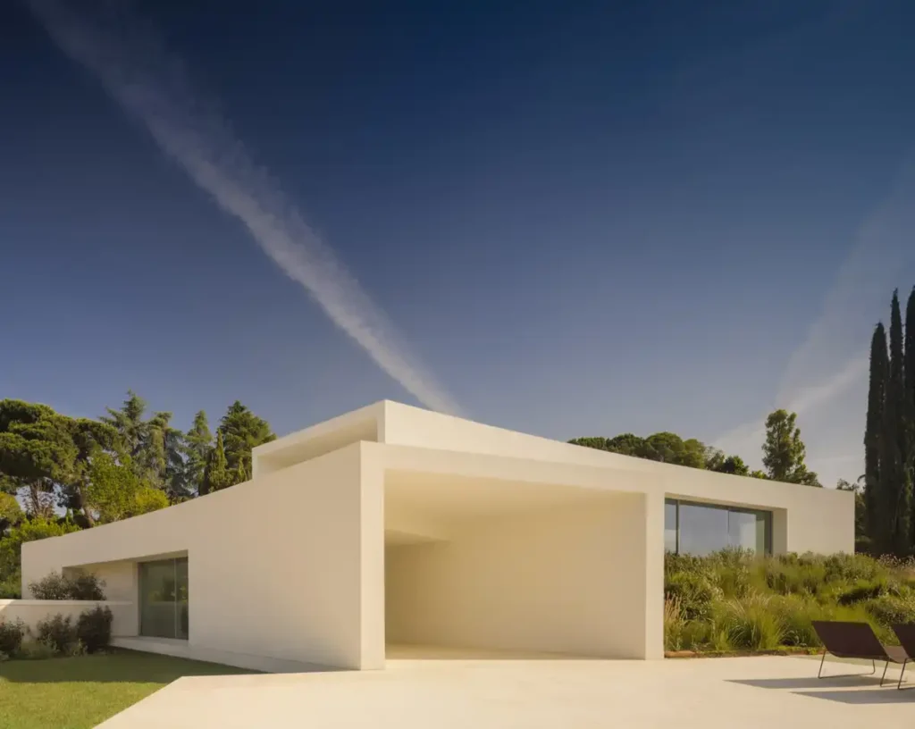 A house that melts into the garden: a modern villa in Madrid blending white concrete walls and green spaces through wide openings and open voids.