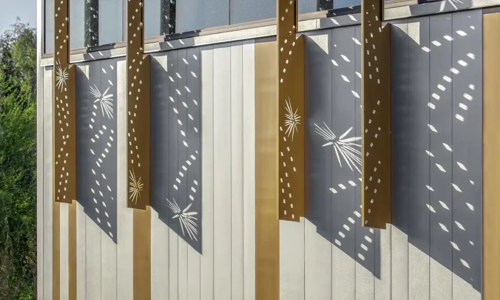 تقرّب من واجهة المبنى  للمعارض في مركز هازل هير للعلوم النباتية المرحلة الثانية، ويظهر الشاشات المعدنية المثقوبة التي تُلقي ظلالًا هندسية على ألواح رأسية بيضاء تحت ضوء الشمس المباشر.