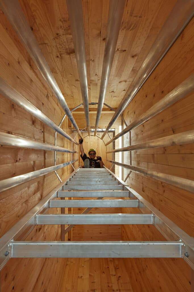 Construction-phase view inside the mass timber fire station, showing a worker on a metal staircase within the exposed timber frame.