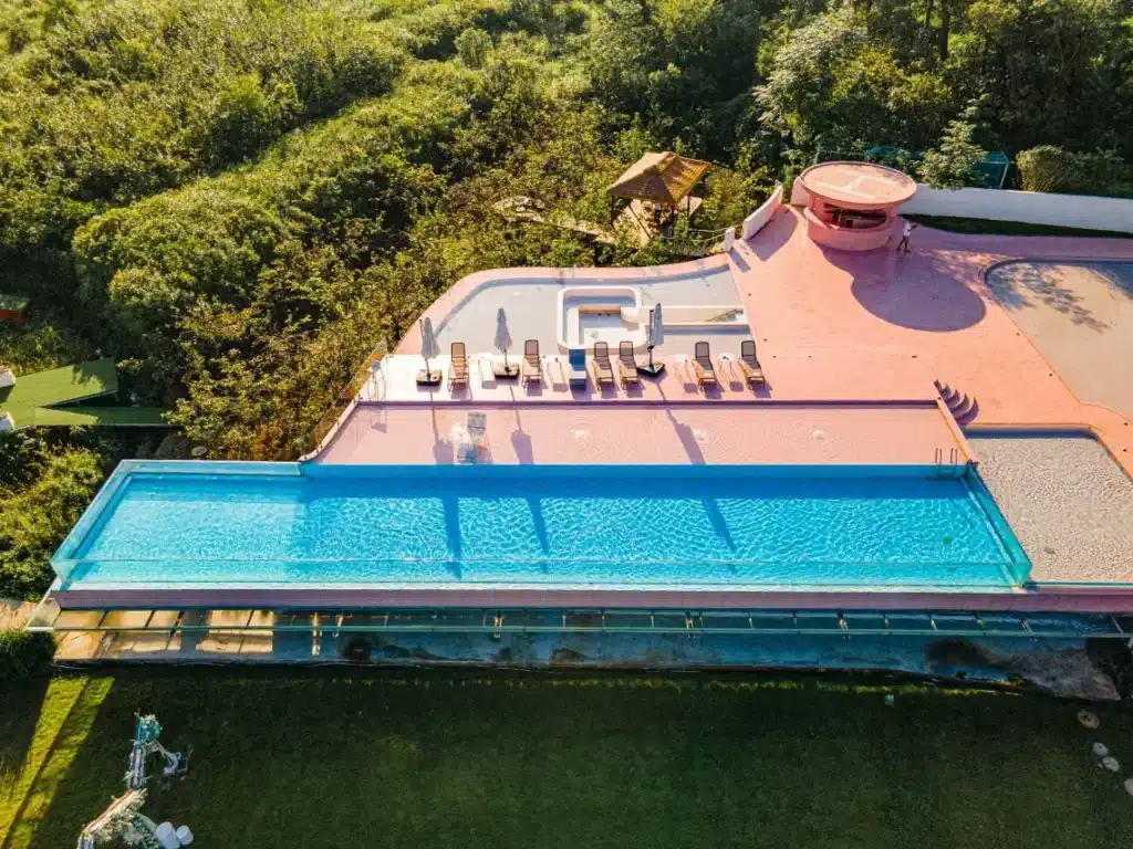 Avatar like views of LS Hotel in Guilin showing a rooftop infinity pool with glass edges, surrounded by lush greenery and featuring sun loungers and a pink circular structure.