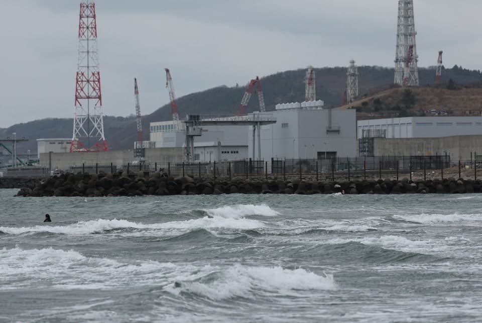 Coastal view illustrating the nuclear architecture of Kashiwazaki-Kariwa Plant, with turbulent waves, breakwaters, and transmission towers rising above hills after Fukushima.
