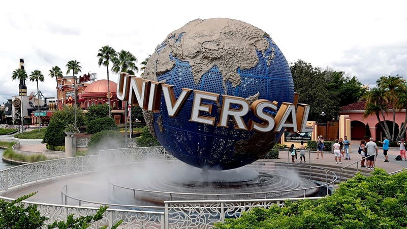 تمثال الكرة الأرضية الأيقوني لـ Universal Studios عند مدخل Universal Orlando Resort، محاط بالضباب وأشجار النخيل تحت سماء غائمة.