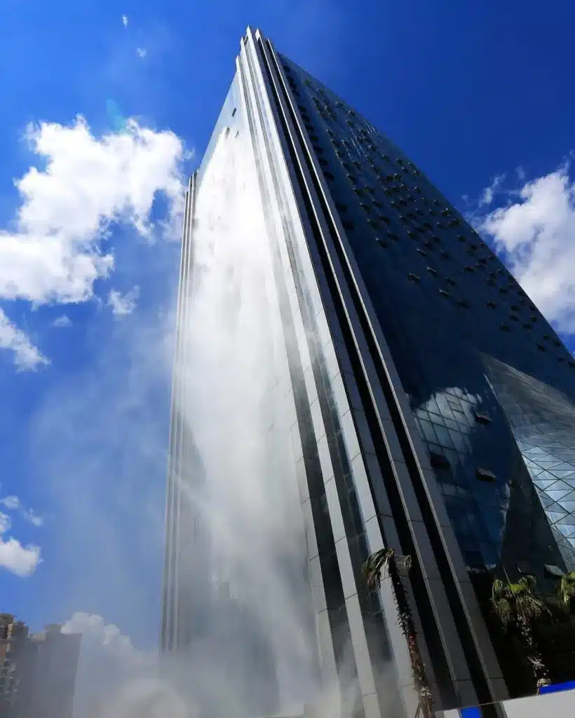 لقطة من الأسفل ناطحة سحاب بشلال ليبيان الدولي في قوييانغ، الصين، يُظهر شلاله المصطنع بطول 108 أمتار وهو يتدفق على واجهته الزجاجية أمام سماء زرقاء صافية مع بعض السحب.