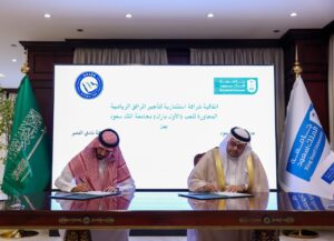 Two officials signing a memorandum of understanding for the Al-Nassr training complex at King Saud University, flanked by Saudi and university flags.