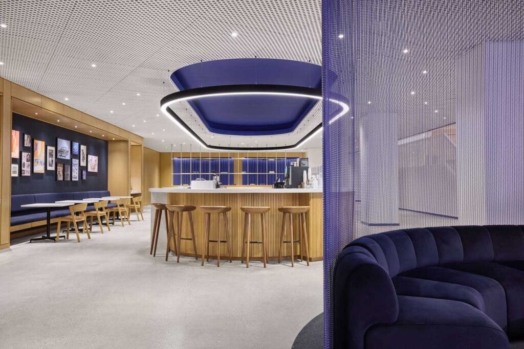 منطقة استراحة وبار حديثة داخل الحرم المركزي لشركة فورد، تضم بارًا خشبيًا منحنيًا بإضاءة زرقاء معلقة، ومقاعد من التول البحري، وسقفًا مثقبًا، محاطة بشاشة شبكية زرقاء لامعة.