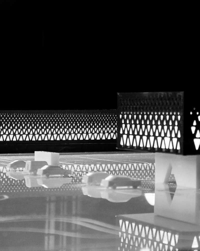 Black and white architectural model of the House Sports Complex, showcasing its perforated facade pattern and spatial relationship to adjacent parking and access areas.