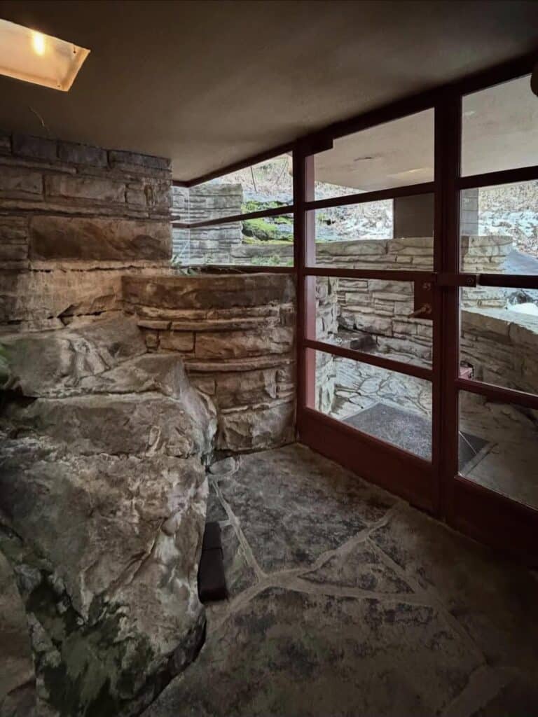 Natural rock formation integrated into the stone wall and floor inside Fallingwater, viewed through glass doors.