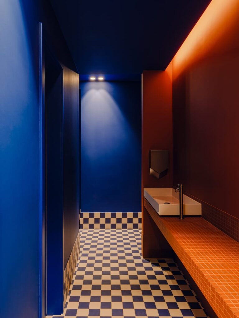 Deep blue corridor with checkered floor, warmed by a glowing orange wall light.
