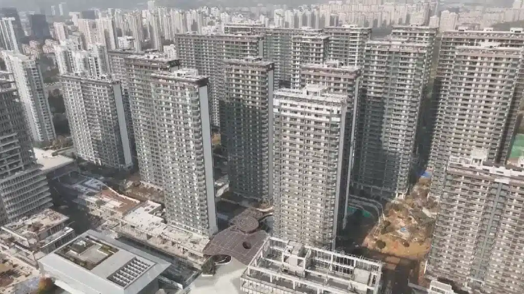 An aerial view of a dense cluster of modern grey high-rise apartment buildings in a city, featuring contemporary architecture and multi-story glass facades.