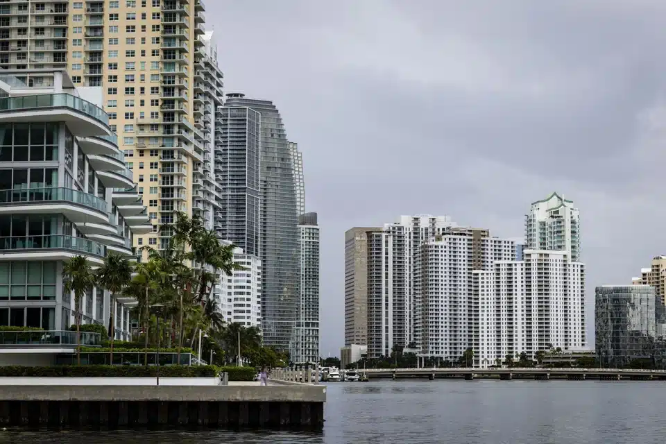 A view from the water of a dense cluster of high-rise luxury apartment buildings and condominiums lining a city waterfront under an overcast sky.