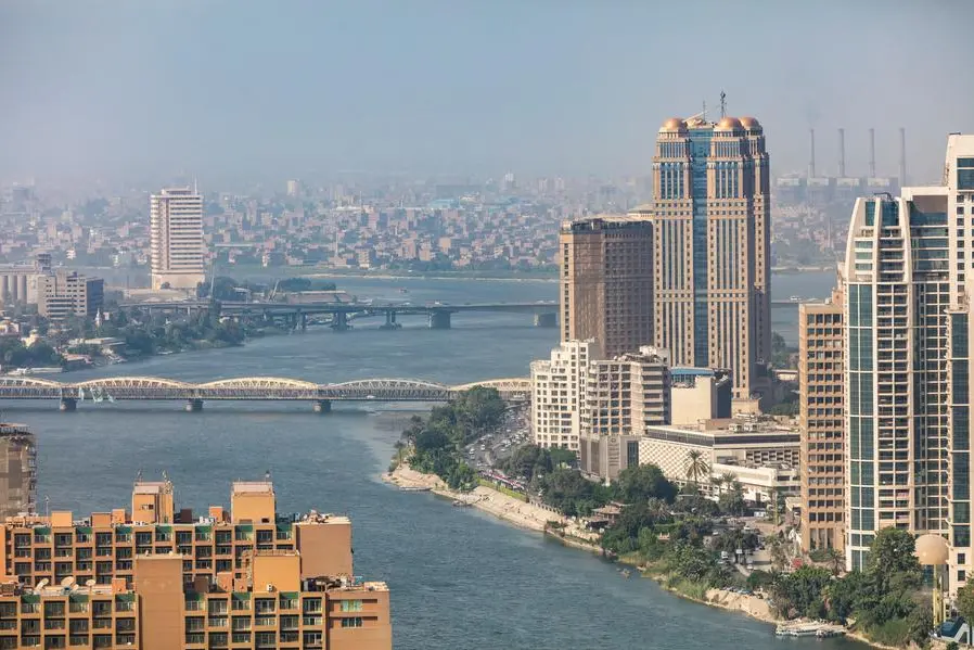 High-angle panoramic view of the Nile River in Cairo, Egypt, featuring the iconic Nile City Towers, bridges, and a dense cityscape under a clear sky.