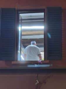 Dark wooden window frame looking into a warm interior with a man, embodying the human dimension of architecture.