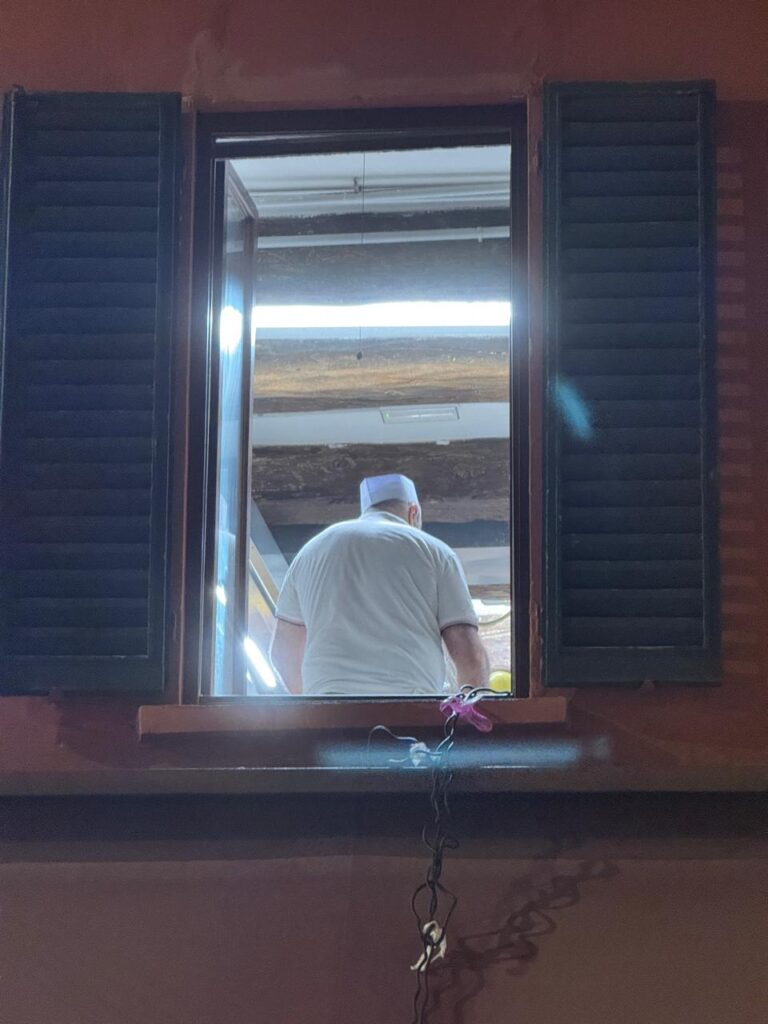 Dark wooden window frame looking into a warm interior with a man, embodying the human dimension of architecture.
