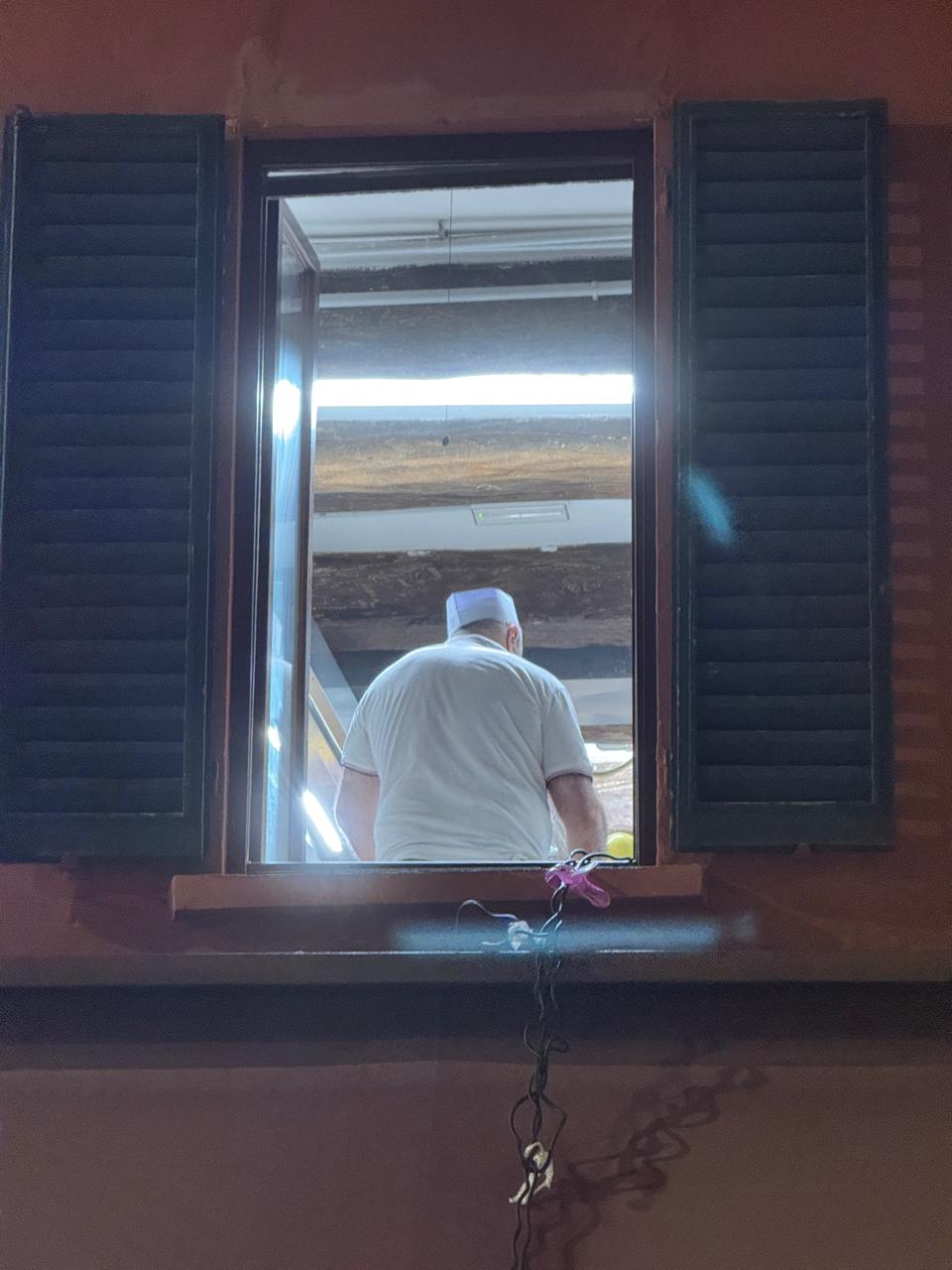 Dark wooden window frame looking into a warm interior with a man, embodying the human dimension of architecture.