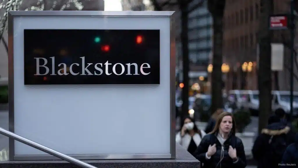 A close-up of a sleek Blackstone corporate sign on a city street with pedestrians walking in the blurred background.