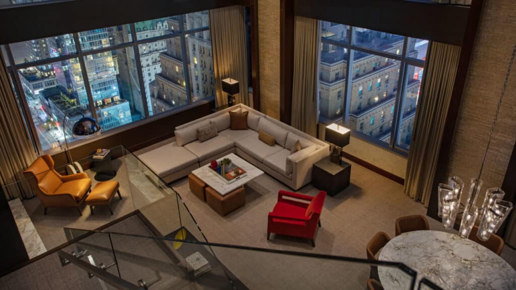 منطقة معيشة في جناح فاخر على السطح في فندق إنتركونتيننتال نيويورك تايمز سكوير مع نوافذ كبيرة تطل على المدينة ليلاً.