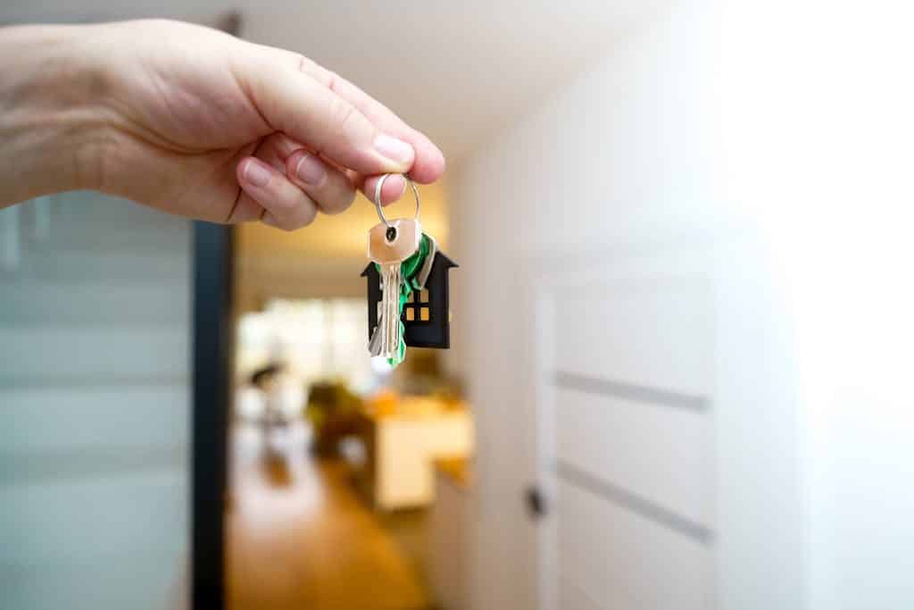A hand holding house keys inside a modern apartment, symbolizing new property ownership or rental.