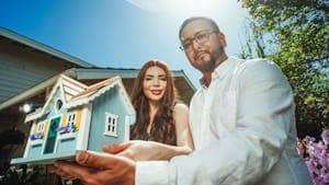 A happy couple holding a miniature house model outdoors, symbolizing new home ownership.