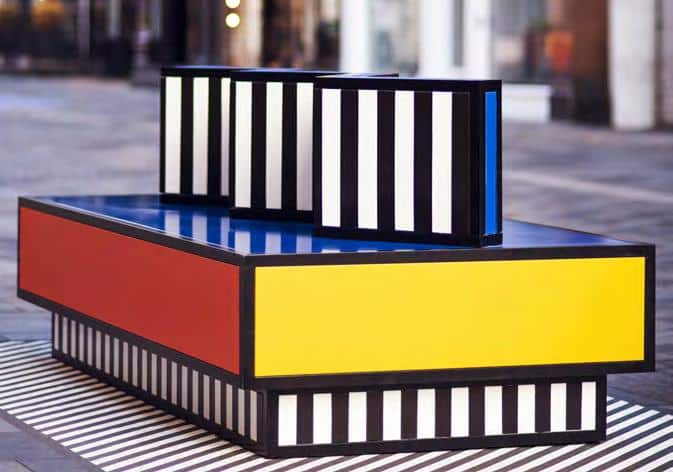 Geometric sculptural steel bench in vibrant pink, blue, and black stripes from the Walala Lounge public art installation by Camille Walala in Bentonville, Arkansas.