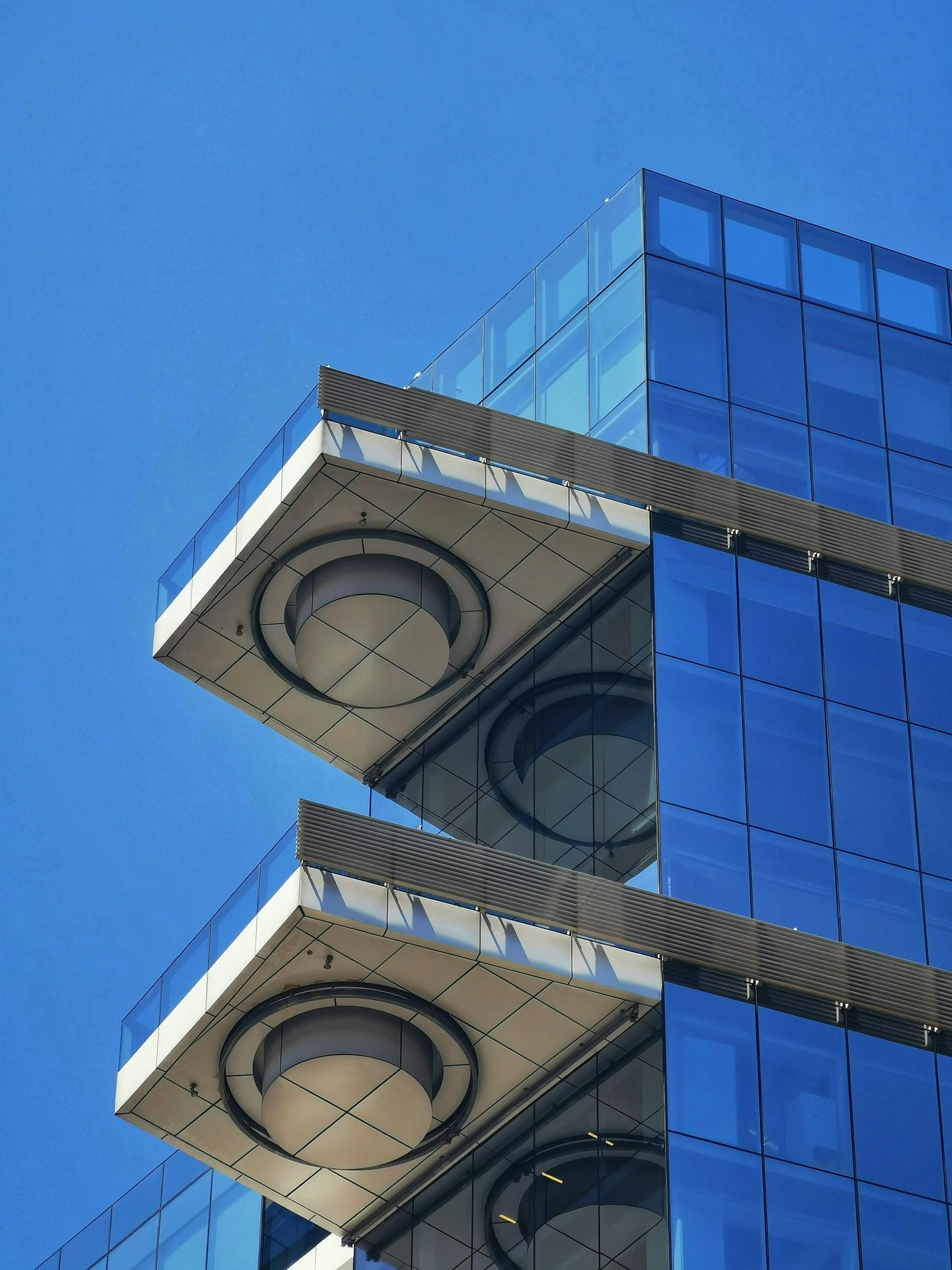 Close-up of a modern glass building with striking geometric architectural elements against a clear blue sky.