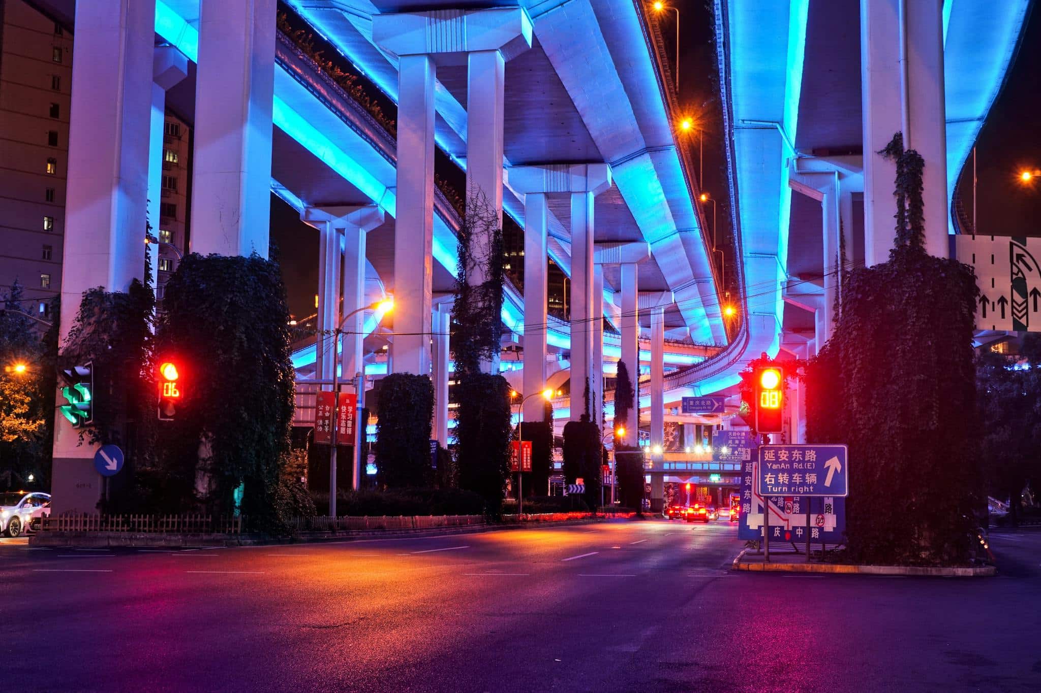 Colorful night scene under Shanghai's illuminated flyovers with vivid blue and red lighting.
