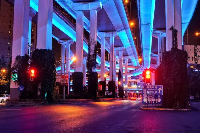 Colorful night scene under Shanghai's illuminated flyovers with vivid blue and red lighting.