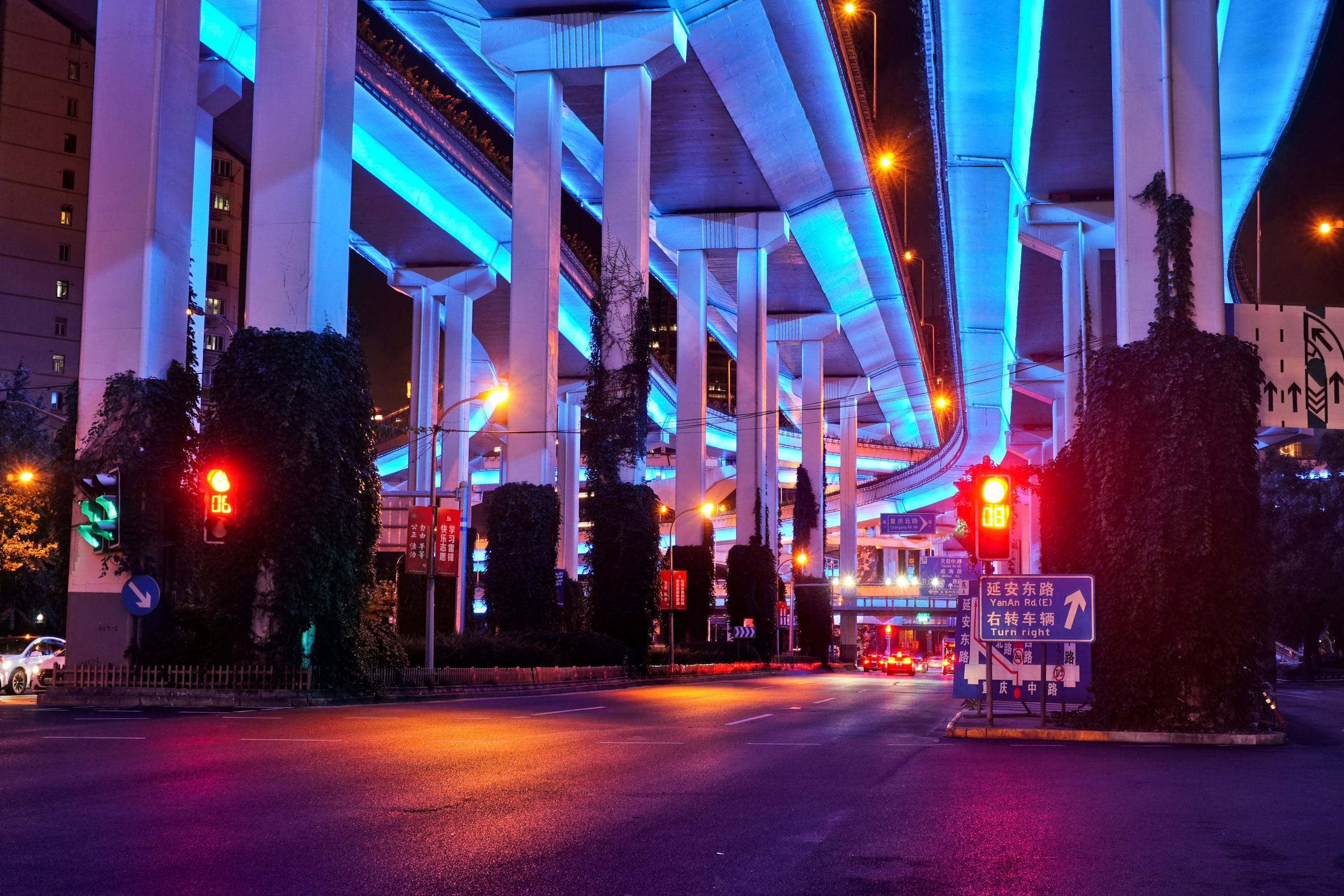 Colorful night scene under Shanghai's illuminated flyovers with vivid blue and red lighting.