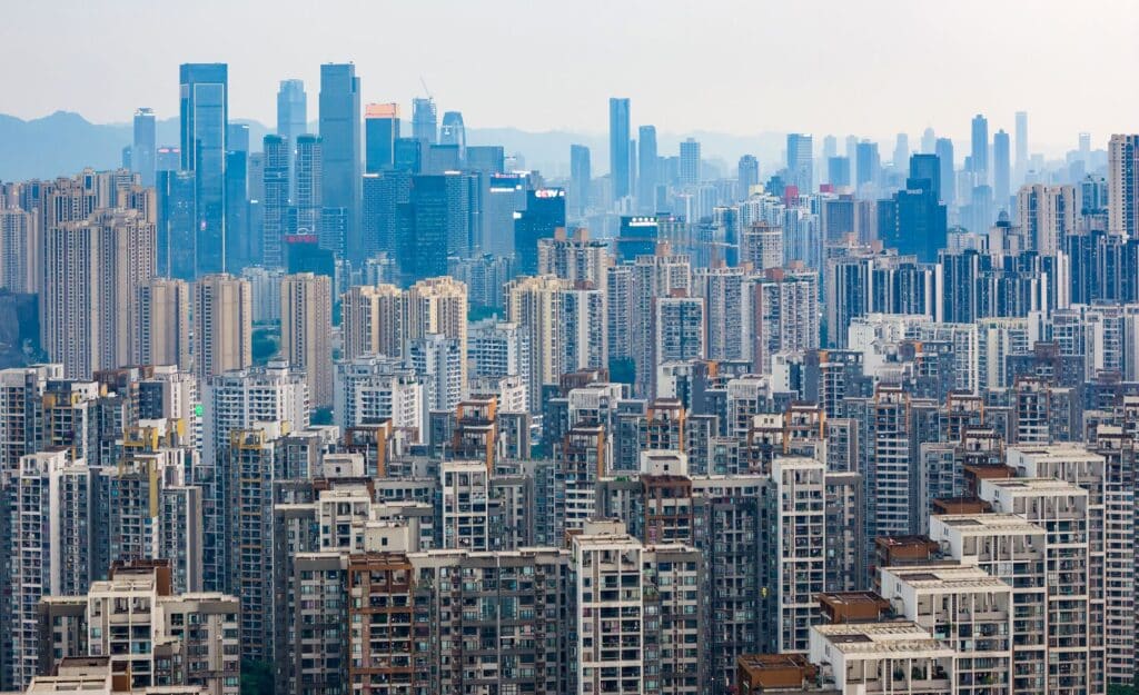 A wide, dense urban skyline where a mass of high-rise residential apartment buildings dominates the foreground, backed by taller, modern commercial skyscrapers in the distant haze.