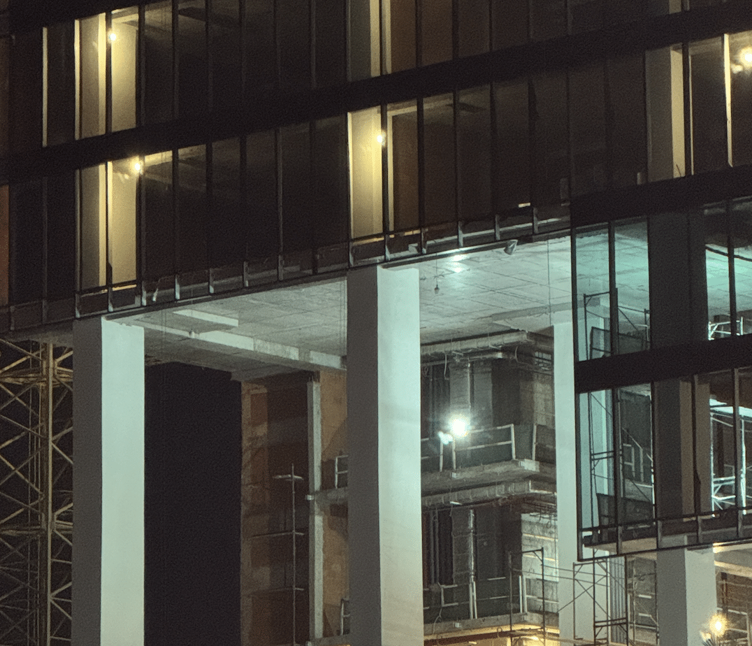Nighttime construction view of a modern multi-story building, highlighting the installation of the glass curtain wall and illuminated concrete structure.