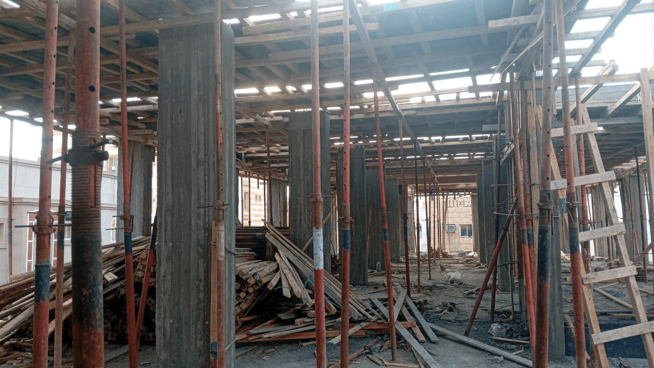 Interior view of an active construction site showing reinforced concrete columns, wooden slab formwork, and steel shoring props.