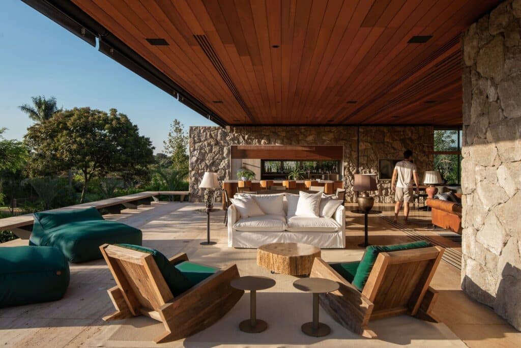 Large shaded terrace at Stone House with comfortable white sofas, wooden armchairs, and a view of the lush garden.