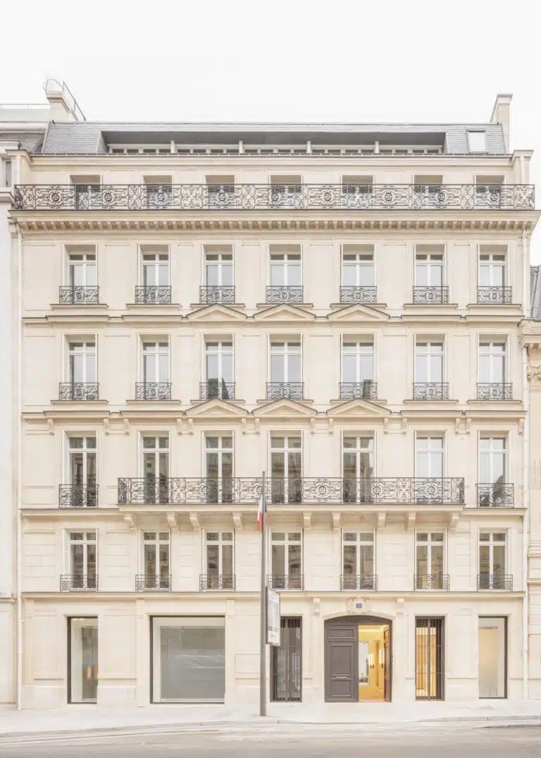 A full-view shot of a classic Haussmannian historic building facade in Paris, featuring ornate iron balconies and limestone walls, restored by Barthélémy Griño.